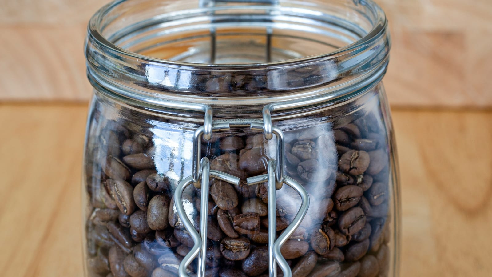 Pote de vidro com tampa hermética cheio de grãos de café, sobre uma tábua de madeira