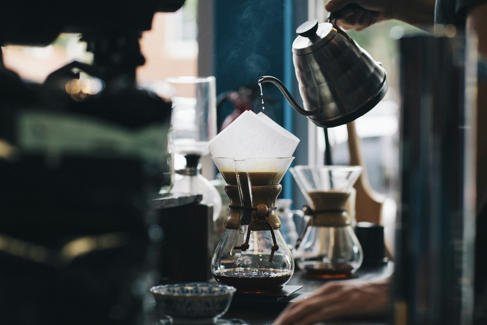 Café sendo coado em um Chemex, com chaleira de bico fino despejando água sobre o filtro