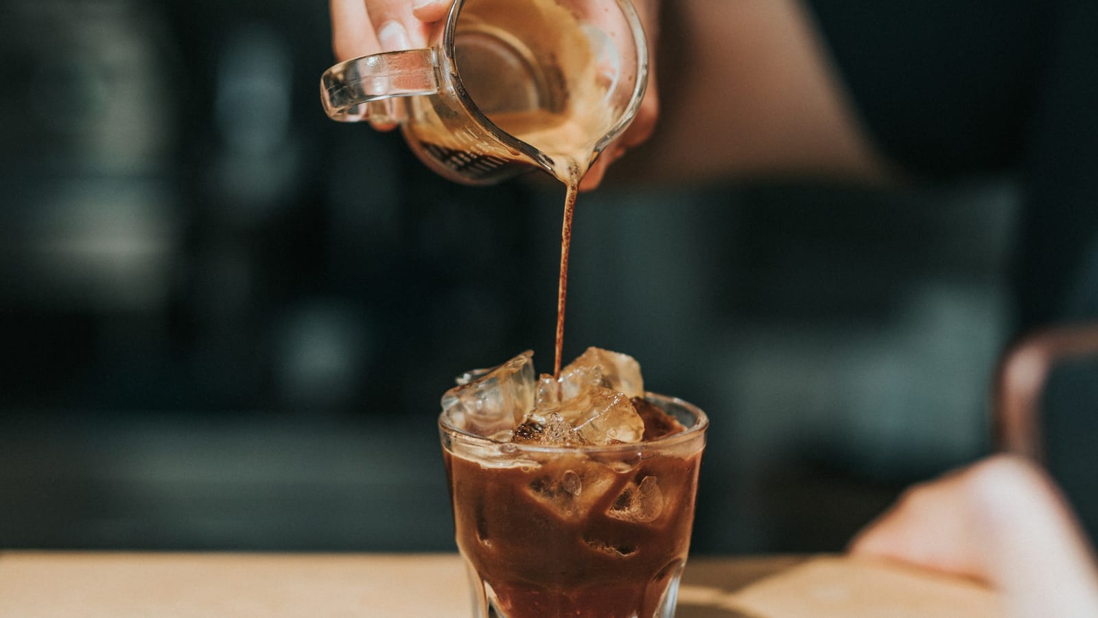 Café sendo despejado de uma jarrinha em um copo com gelo
