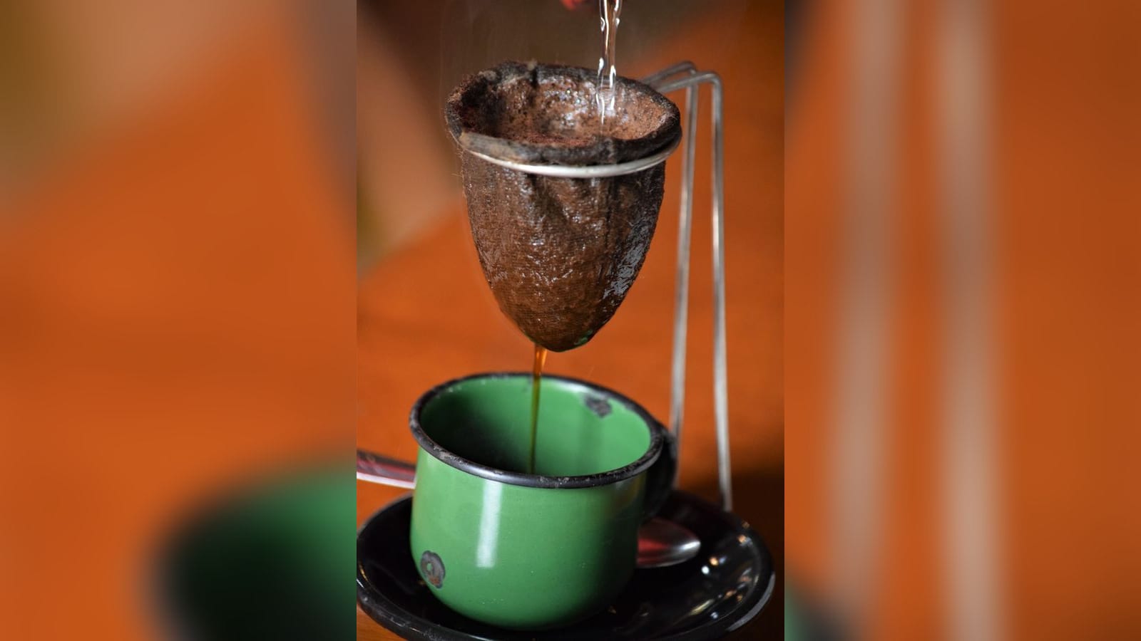 Café coado em coador de pano pingando em uma caneca esmaltada verde