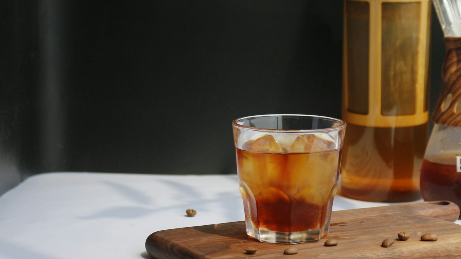 Copo de vidro com café cold brew e gelo ao lado de uma garrafa de infusão a frio, sobre uma tábua de madeira