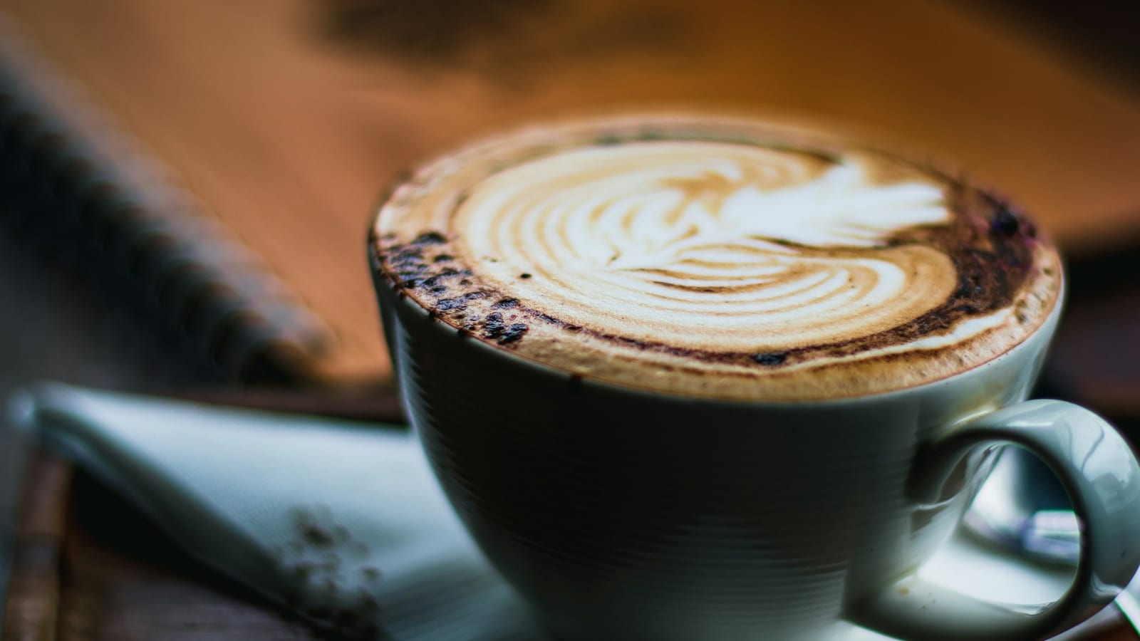Cappuccino com arte na espuma em uma xícara verde-acinzentada, em close