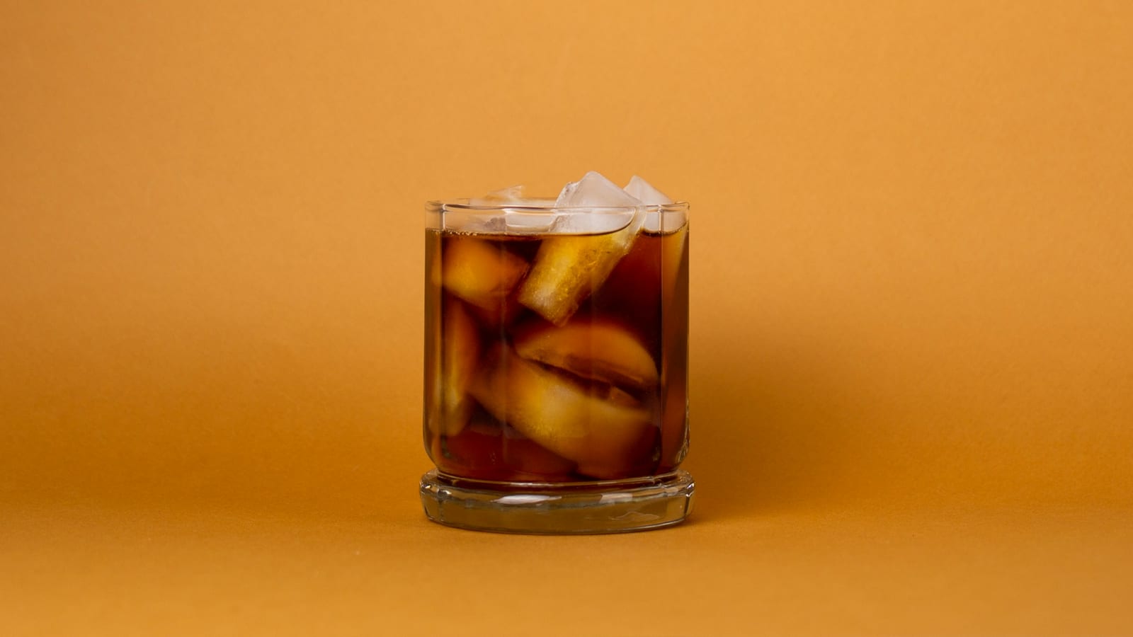 Copo baixo de café cold brew com cubos de gelo sobre fundo cor de laranja