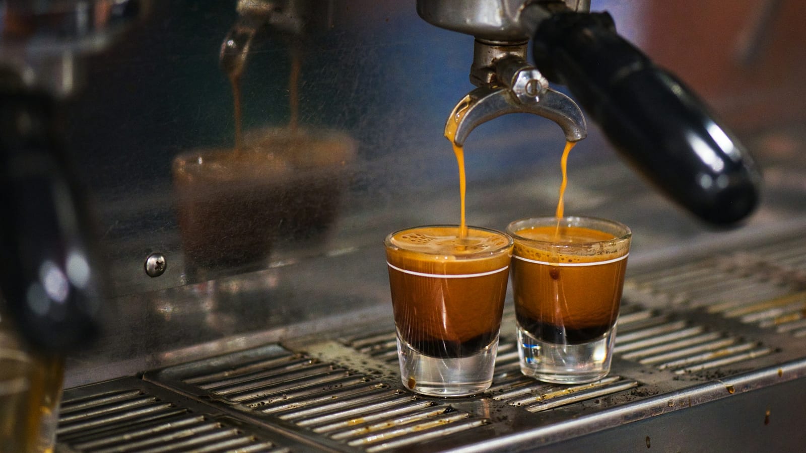 Dois copinhos de vidro recebendo espresso de uma máquina, com crema dourada